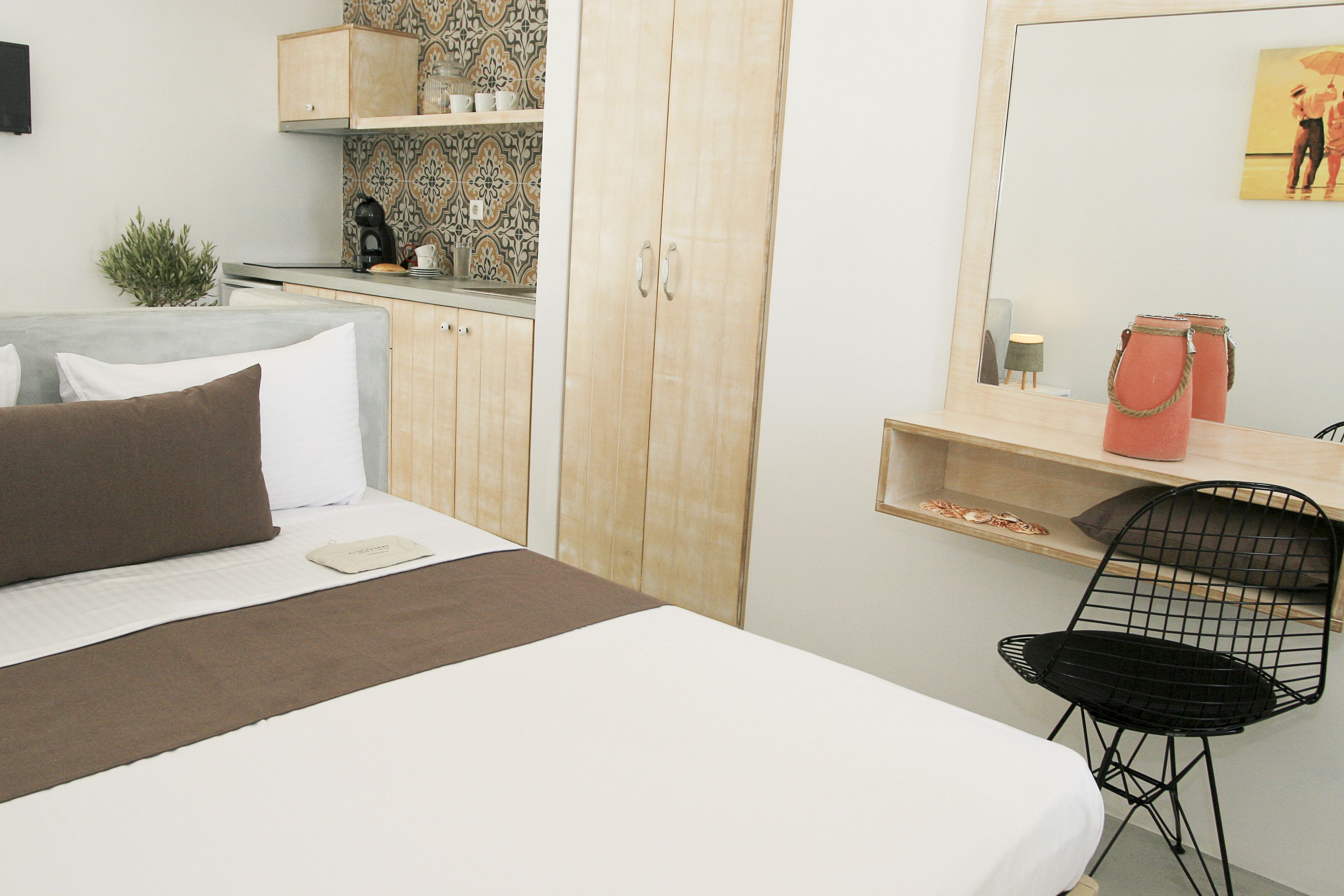 Quarto com cama, escrivaninha, cadeira, guarda-roupa e área de cozinha com cafeteira.