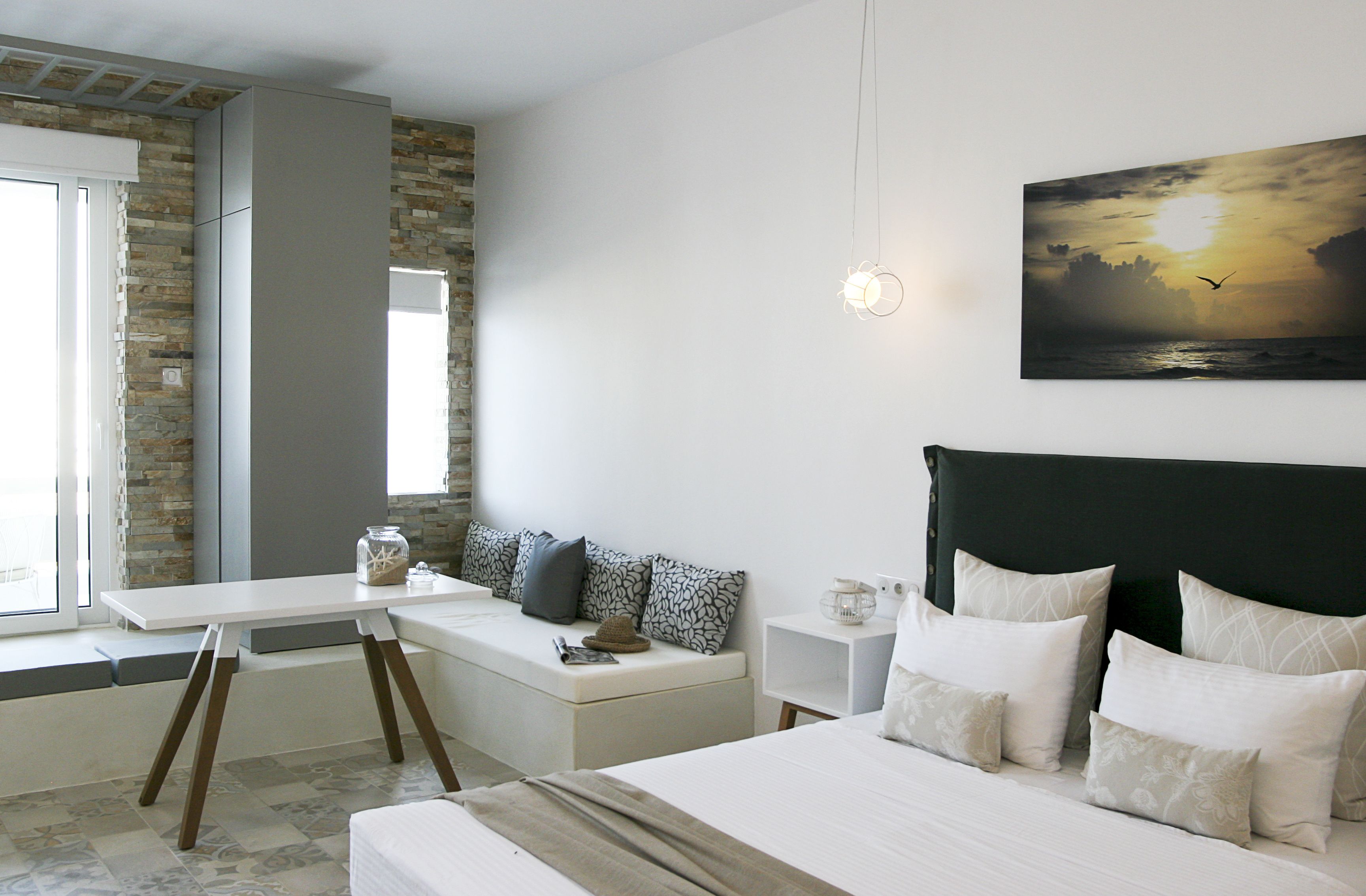 Un dormitorio moderno con una cama grande, una zona de estar con una mesa y vistas al atardecer a través de la ventana.