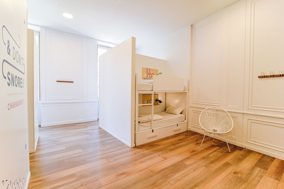 Una habitación con literas, una silla blanca y un armario blanco.