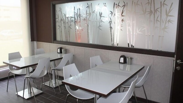 A modern dining area with glass tables and white chairs, a large decorative bamboo wall, and a view of the outside. - Albergue Credencial - Hostel (Sarria)