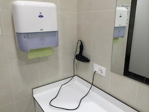 A restroom with a white sink, a paper towel dispenser, and a hand dryer.