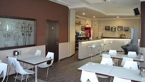 A modern restaurant with white tables and chairs, a bar area, and a decorative wall with bamboo artwork. - Albergue Credencial - Hostel (Sarria)