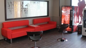 A modern hotel lobby with a red sofa and two black chairs, a large abstract painting on the wall, and a large screen displaying a silhouette. - Albergue Credencial - Hostel (Sarria)