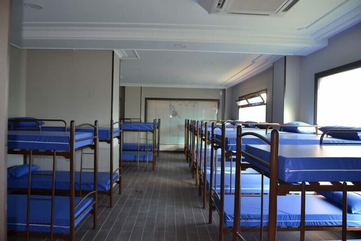 A dormitory room with bunk beds arranged in rows, a tiled floor, and a window providing natural light.