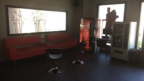A modern living room with a red sofa, two black chairs, a large window with a view, a refrigerator, and a TV. - Albergue Credencial - Hostel (Sarria)