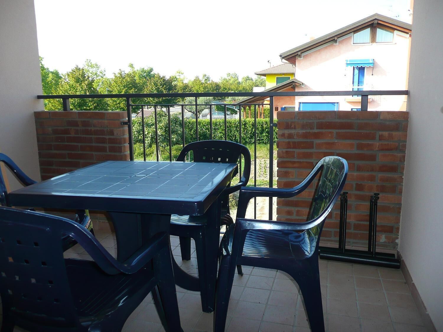 A balcony with a table and chairs, a brick wall, and a view of a building with a blue awning.