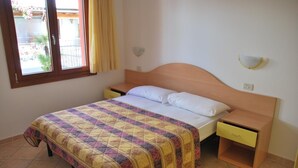 Une chambre à coucher comprenant un lit, deux tables de chevet, une fenêtre avec des rideaux et un luminaire fixé au mur.