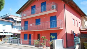 Un immeuble à deux étages doté de balcons, d’une façade rouge et d’une entrée fermée par un portail.