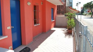 Un bâtiment rouge avec des portes et des fenêtres bleues, un petit balcon orné d’un pot de fleurs et une clôture en métal.