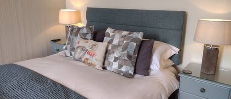 A neatly made bed with a grey headboard, two bedside tables with lamps, and patterned pillows.