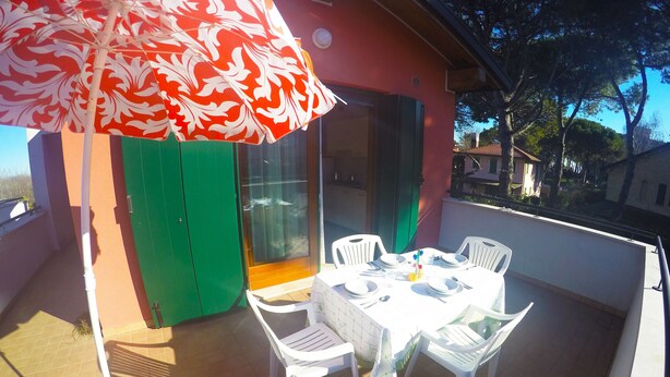 A patio with a table set for dining, surrounded by chairs, and an umbrella providing shade. - Residence Le Piramidi (Caorle)