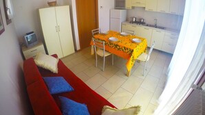 A compact living space with a dining area, kitchenette, and a red sofa with blue cushions. - Residence Le Piramidi (Caorle)