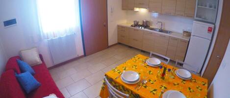 A compact living space with a dining area, kitchenette, and a red sofa with blue cushions.