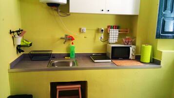 Una cocina pequeña con un lavamanos, un microondas, un tostador y un taburete de madera.