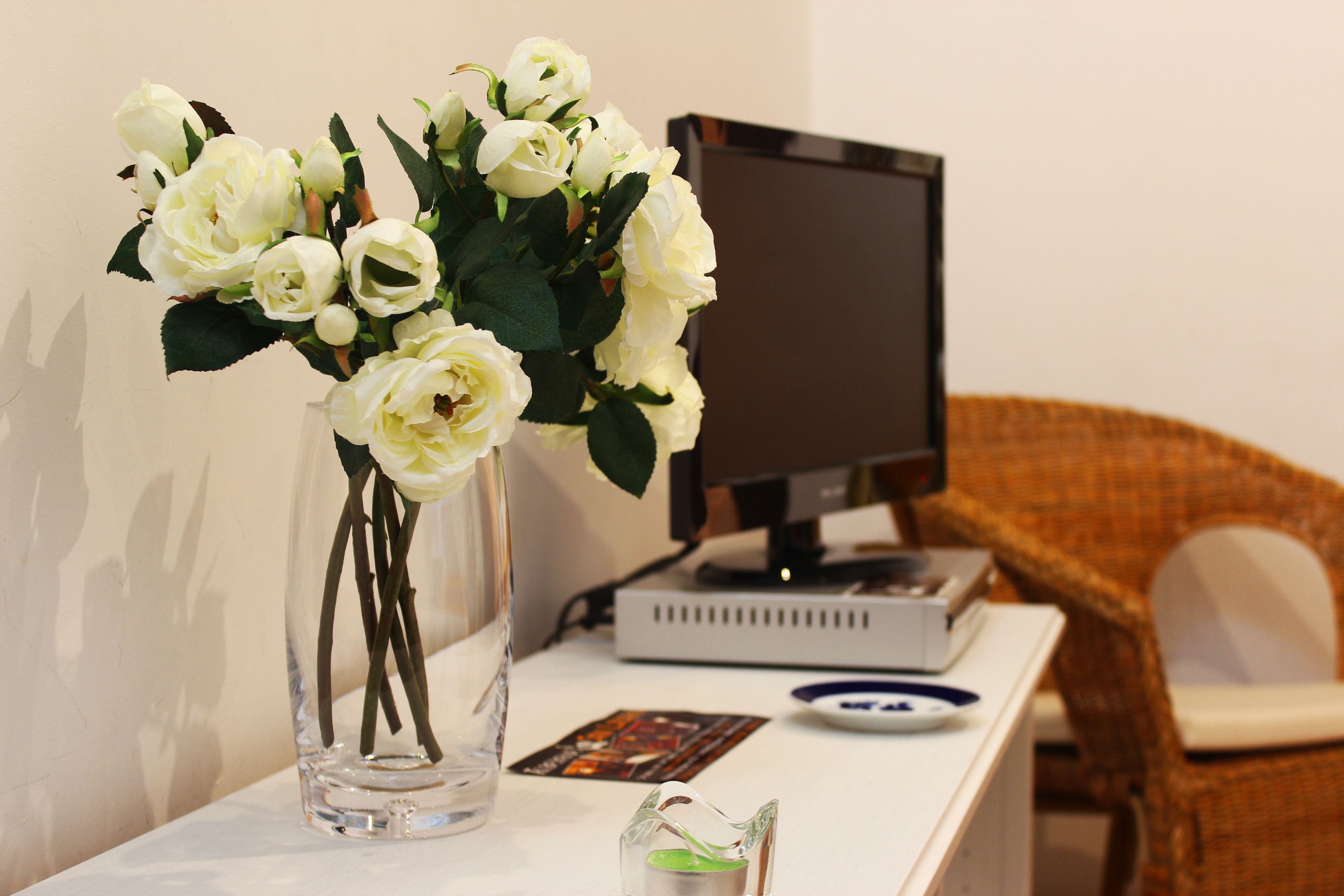 Uma escrivaninha com um vaso de flores brancas, um monitor de computador e um leitor de DVD.