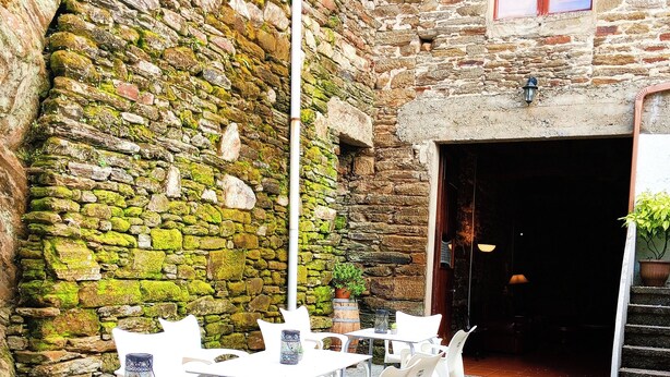 Un área de estar al aire libre con paredes de piedra y un ambiente rústico. Mesas y sillas dispuestas para comer.