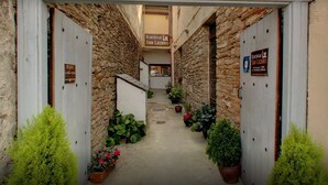 Un estrecho callejón con muros de piedra, plantas en macetas y carteles que indican 'Albergue San Lazaro' y 'Albergue'.