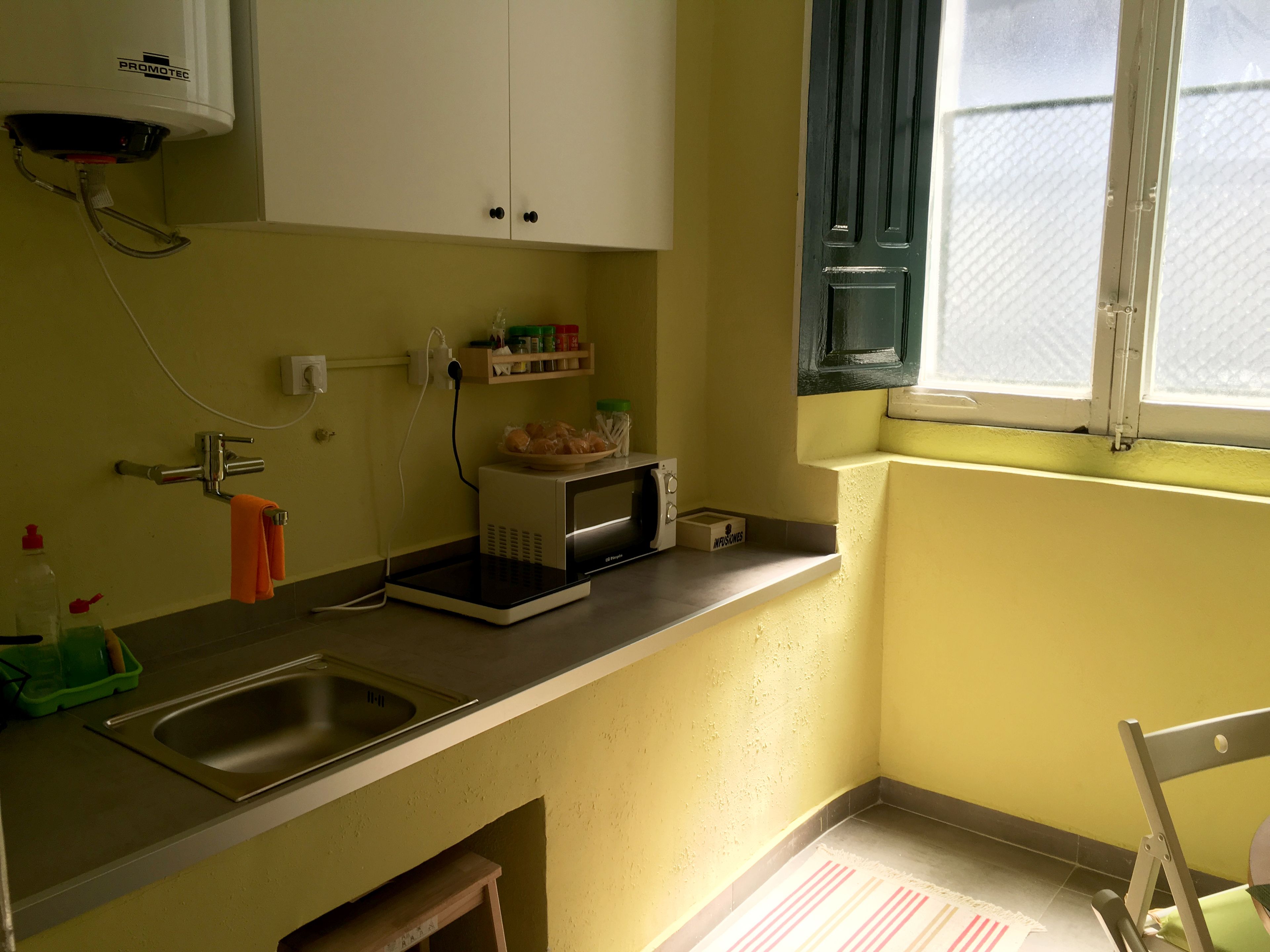 Una cocina pequeña con un lavamanos, un microondas y una ventana.