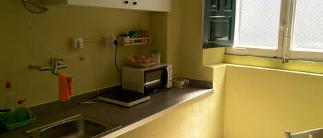 Una cocina pequeña con un lavamanos, un microondas y una ventana.