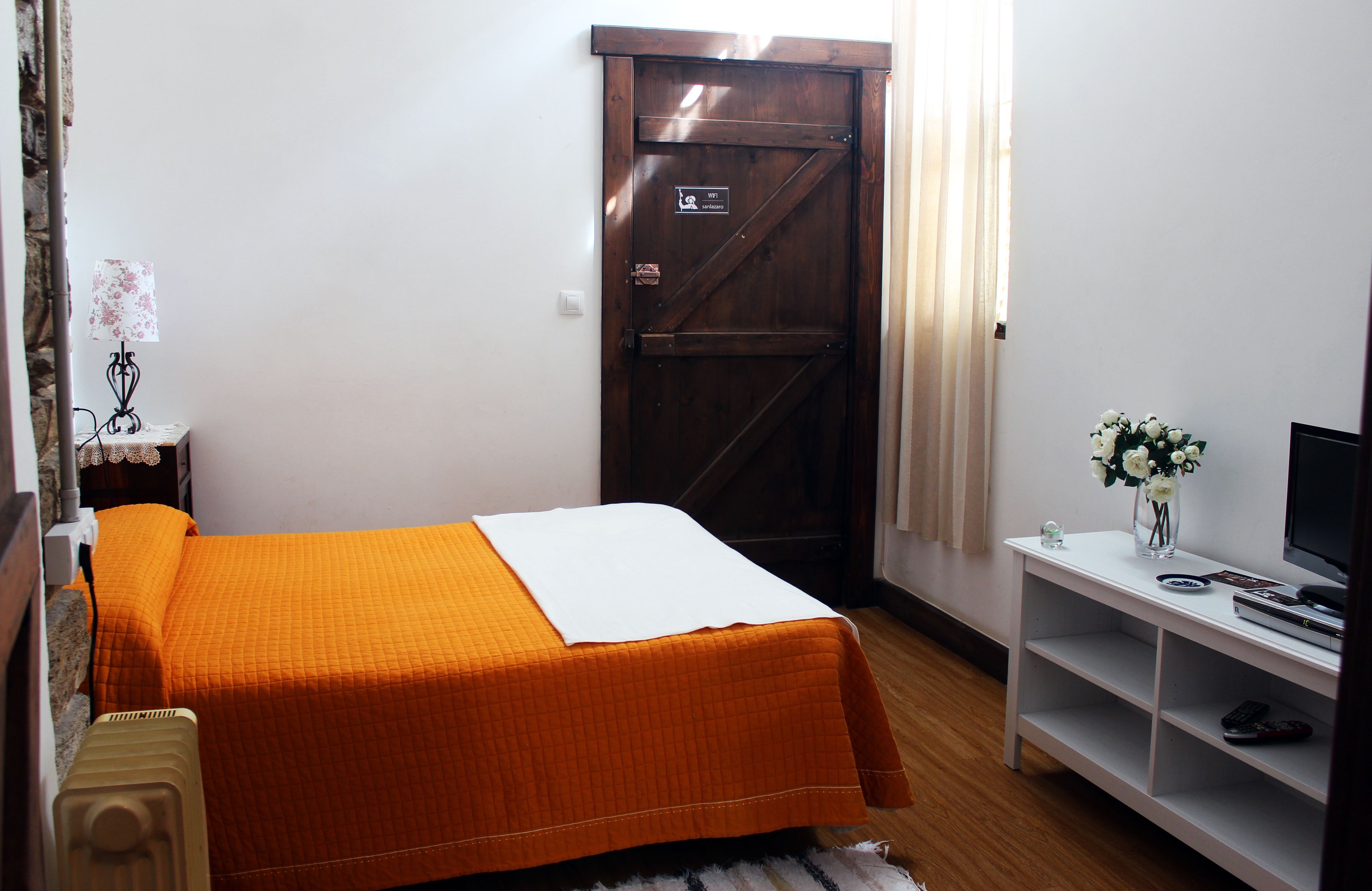 A small, neatly arranged bedroom with a bed, a nightstand, a TV, and a shelf.