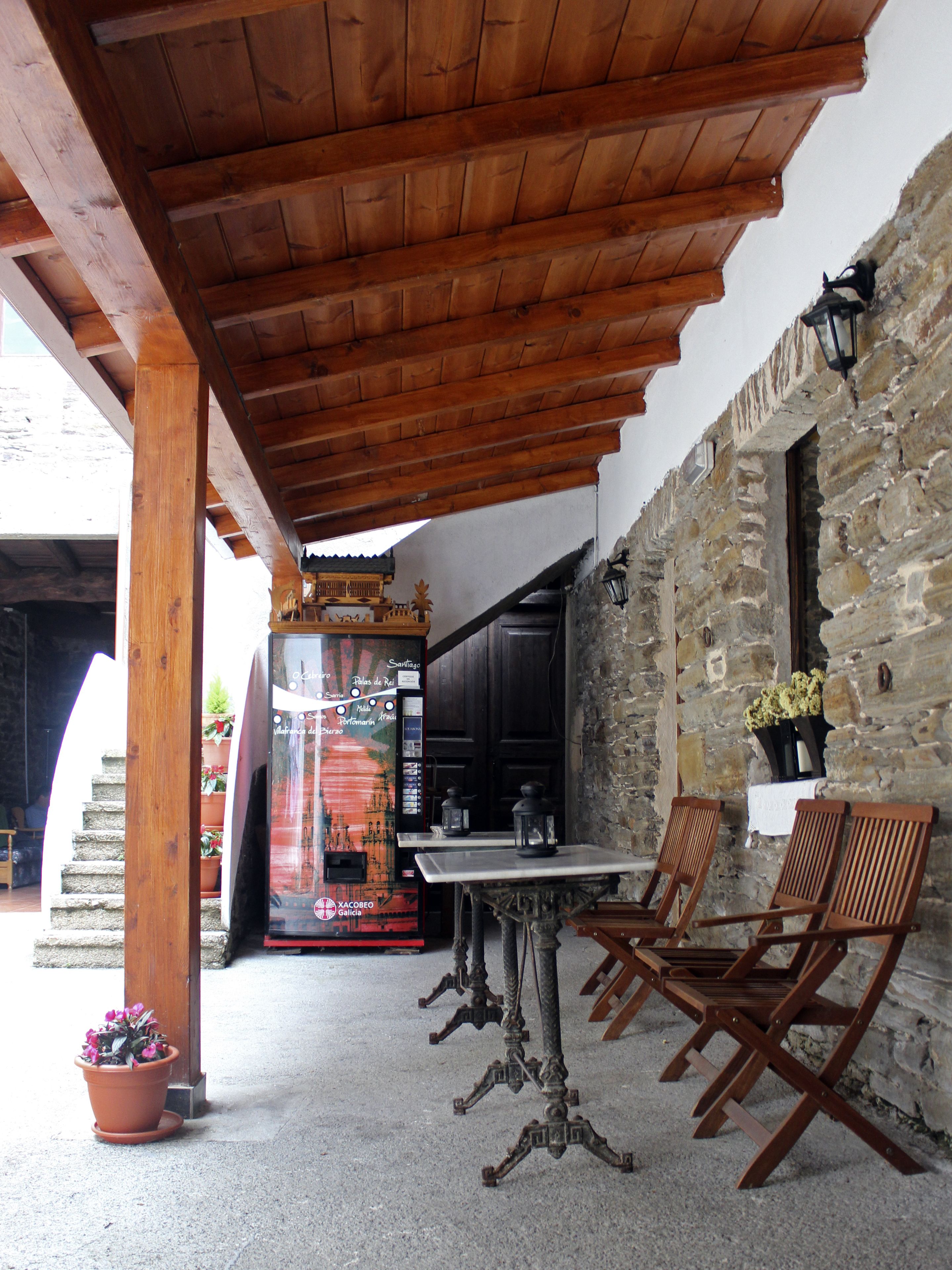 A covered outdoor seating area with a table and chairs, a vending machine, and a stone wall.