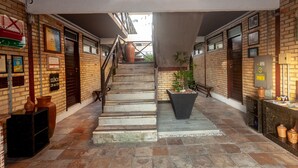 A staircase leading to an upper level, flanked by brick walls with various signs and a large planter with a plant. - Economy Flat (Natal)