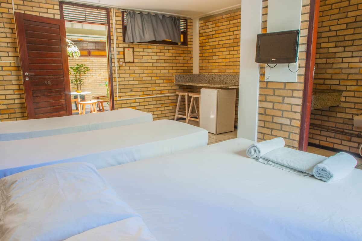A hotel room with two beds, a small kitchenette, a TV, and a brick wall.