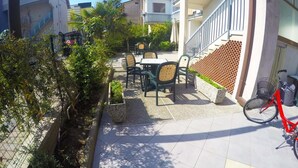 An outdoor patio area with tables and chairs, a bicycle, and a brick wall. - Appartamenti Levante (Caorle)