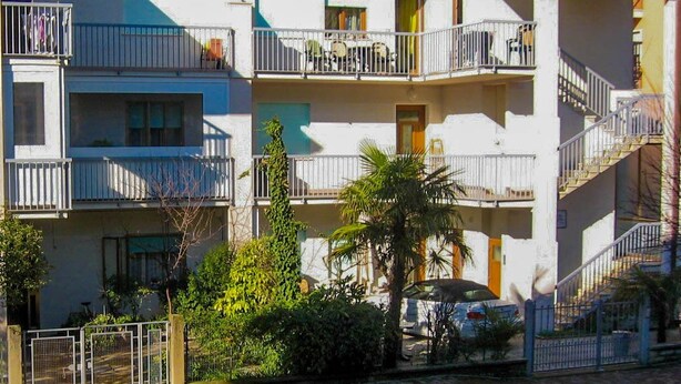 A multi-story residential building with balconies, a car parked in front, and a palm tree. - Appartamenti Levante (Caorle)