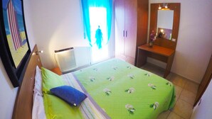 A hotel room with a bed, a bedside table, a mirror, and a window with curtains. - Appartamenti Levante (Caorle)