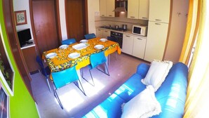 A compact living space with a dining area, kitchenette, and a blue sofa. - Appartamenti Levante (Caorle)