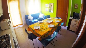 A dining area with a table set for four, a blue sofa, a kitchen area with a stove, and a green accent wall. - Appartamenti Levante (Caorle)