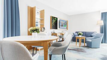 A modern living room with a round wooden table, grey upholstered chairs, a blue sofa, and a small wooden side table with a lamp.