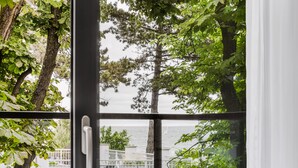 A view through a window with a metal railing, trees, and a body of water in the background. - Hotel Testa (Sopot)