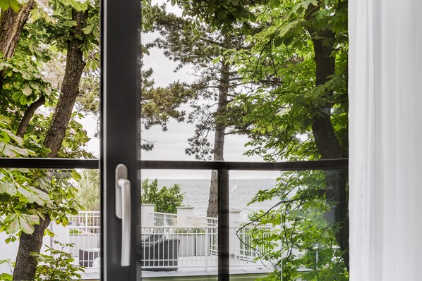 A view through a window with a metal railing, trees, and a body of water in the background. - Hotel Testa (Sopot)