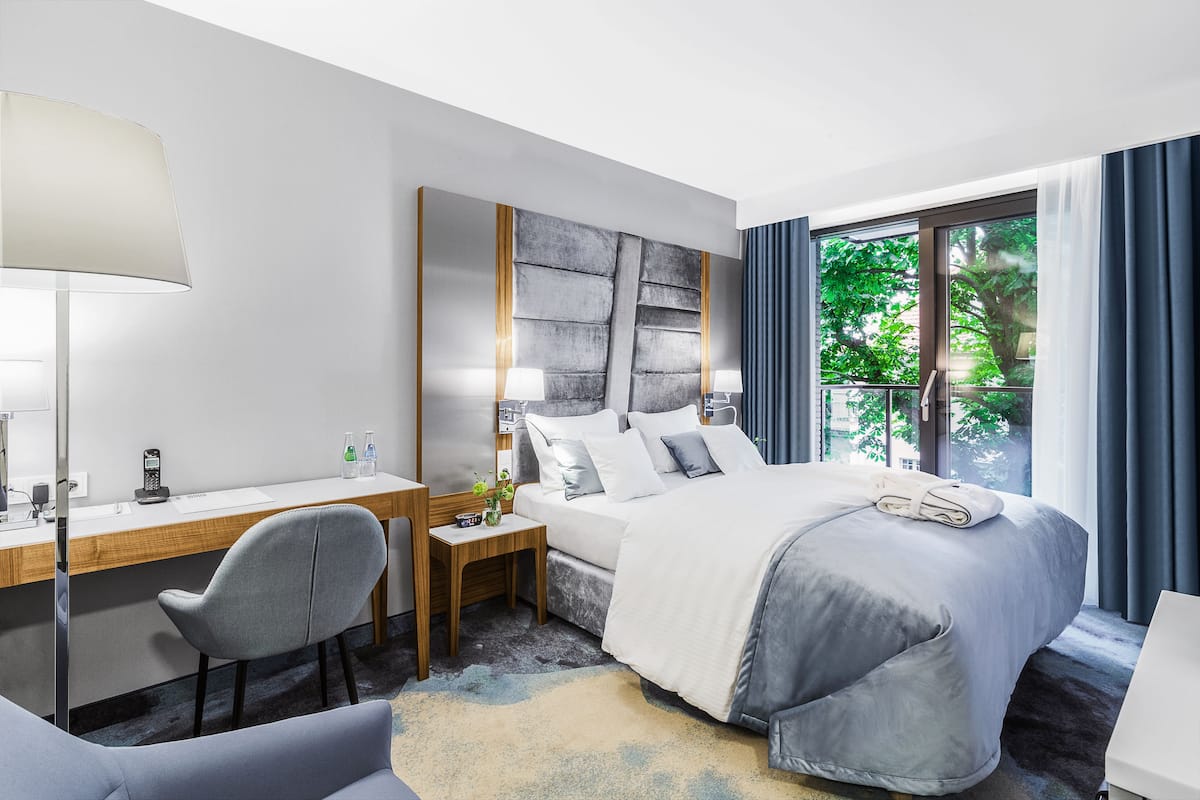 A modern hotel room with a bed, desk, chair, and a large window with curtains.