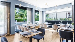 A restaurant with wooden flooring, modern chairs, and tables set for dining. Large windows offer views of greenery outside. - Hotel Testa (Sopot)