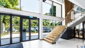 A modern hotel lobby with a glass entrance, a wooden staircase, and a seating area with a table and chairs. - Hotel Testa (Sopot)