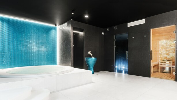 A modern bathroom with a large bathtub, a glass sculpture, and a wooden door leading to a shower area. - Hotel Testa (Sopot)