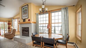A dining area with a round table, four chairs, a fireplace, and large windows with curtains. - Skyport Lodge (Grand Marais)