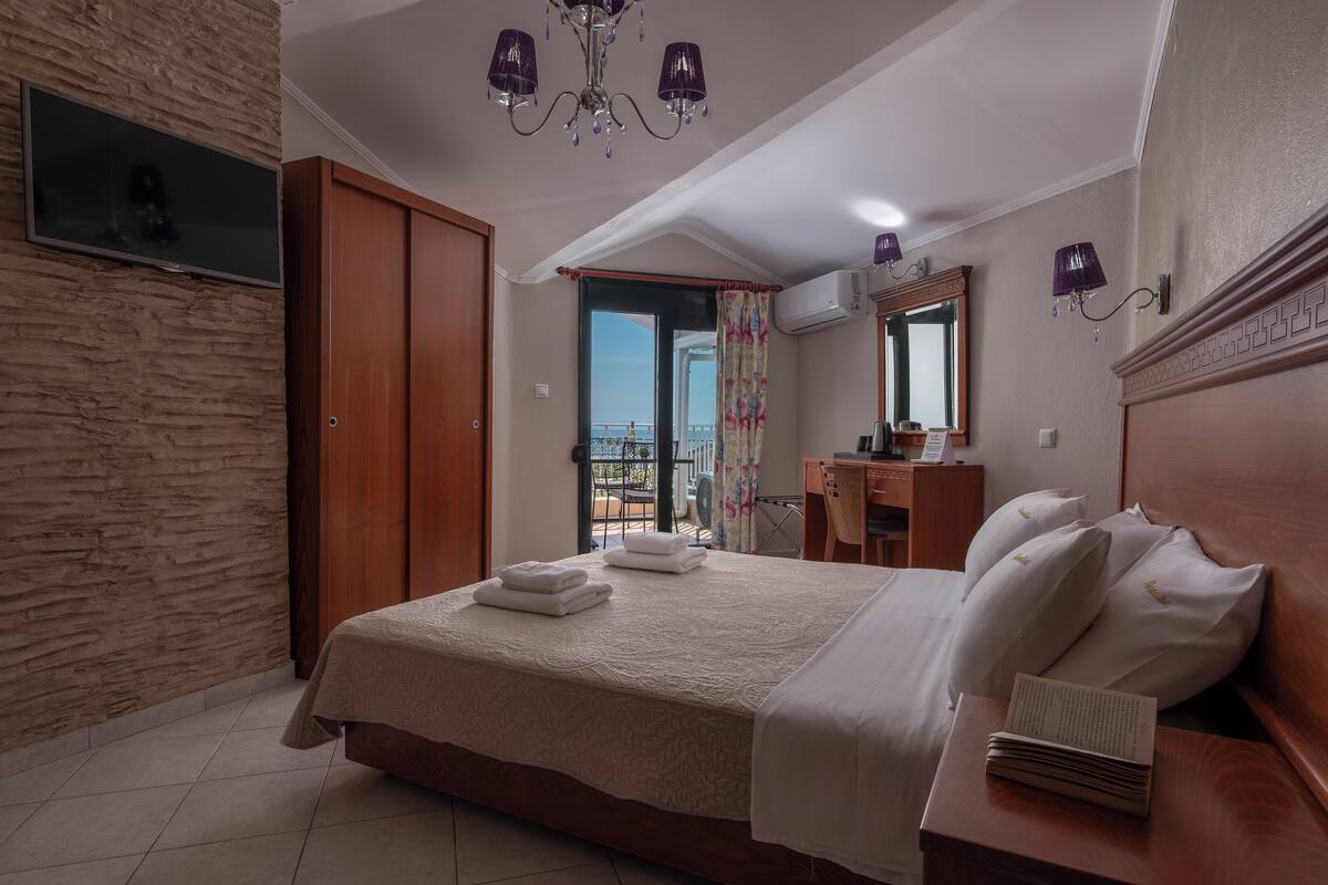Habitación de hotel con una cama grande, un aparador de madera, un tocador con espejo y un balcón con vistas.