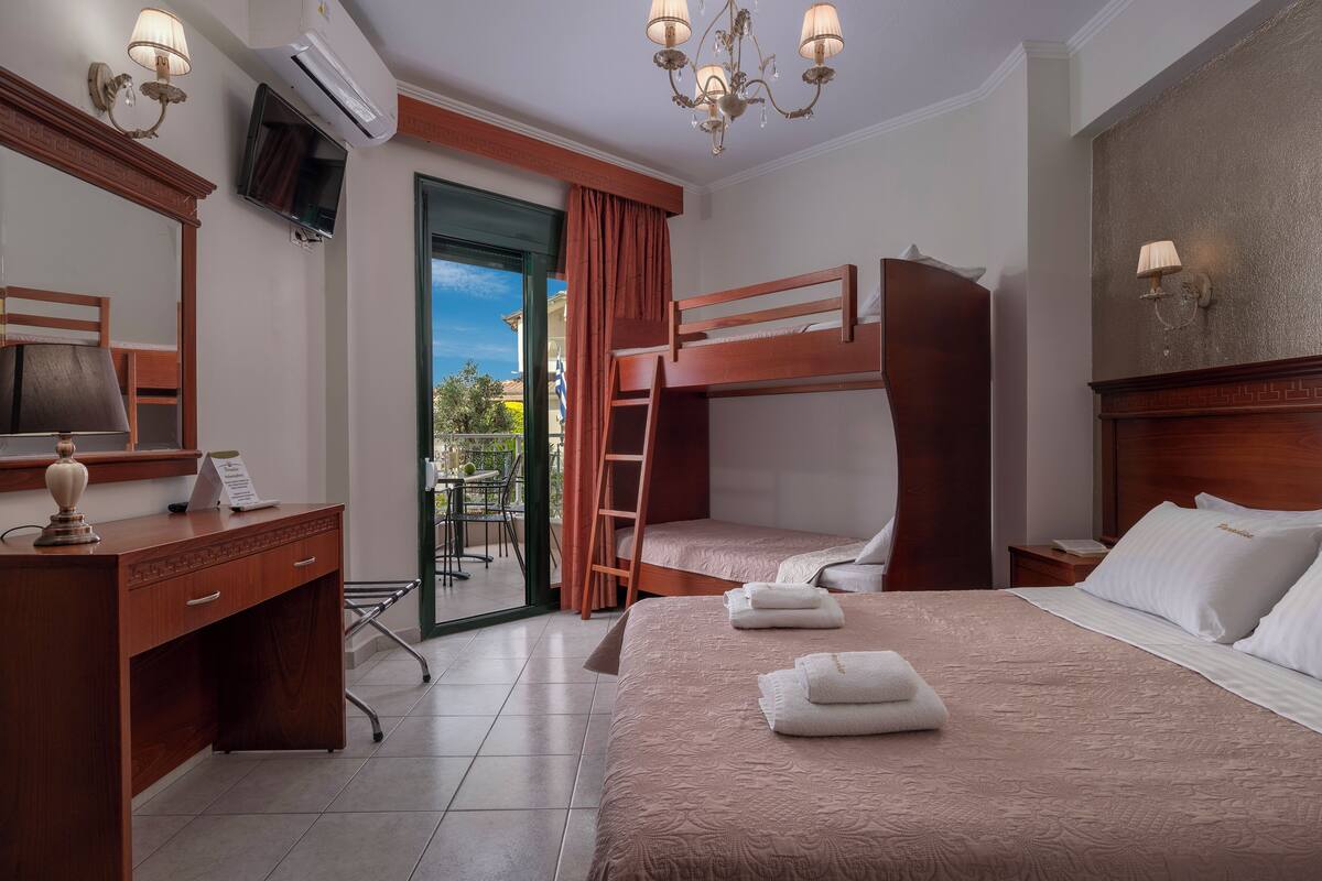 Habitación de hotel con literas, un escritorio con lámpara, un televisor y vistas al exterior.
