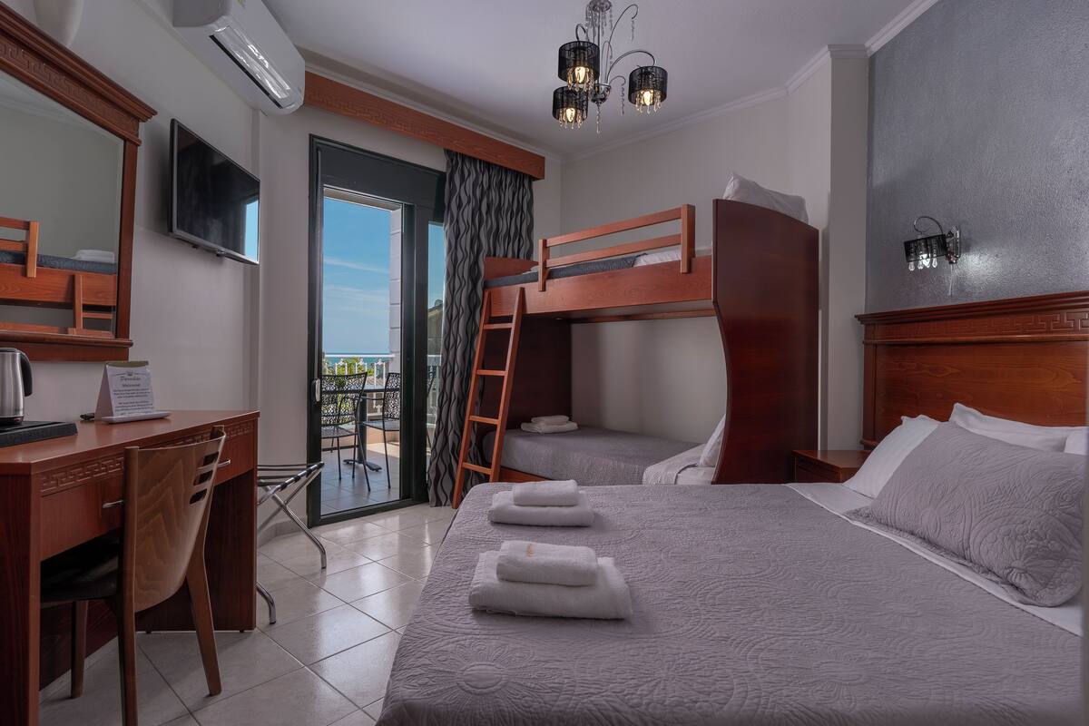 Habitación de hotel con escritorio, dos literas, televisión y balcón con vistas.