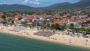 A coastal town with a beach, rows of red-roofed houses, and a mountainous backdrop. - Paradise (Volvi)