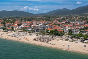 Un pueblo costero con una playa, hileras de casas con tejados rojos y montañas al fondo.