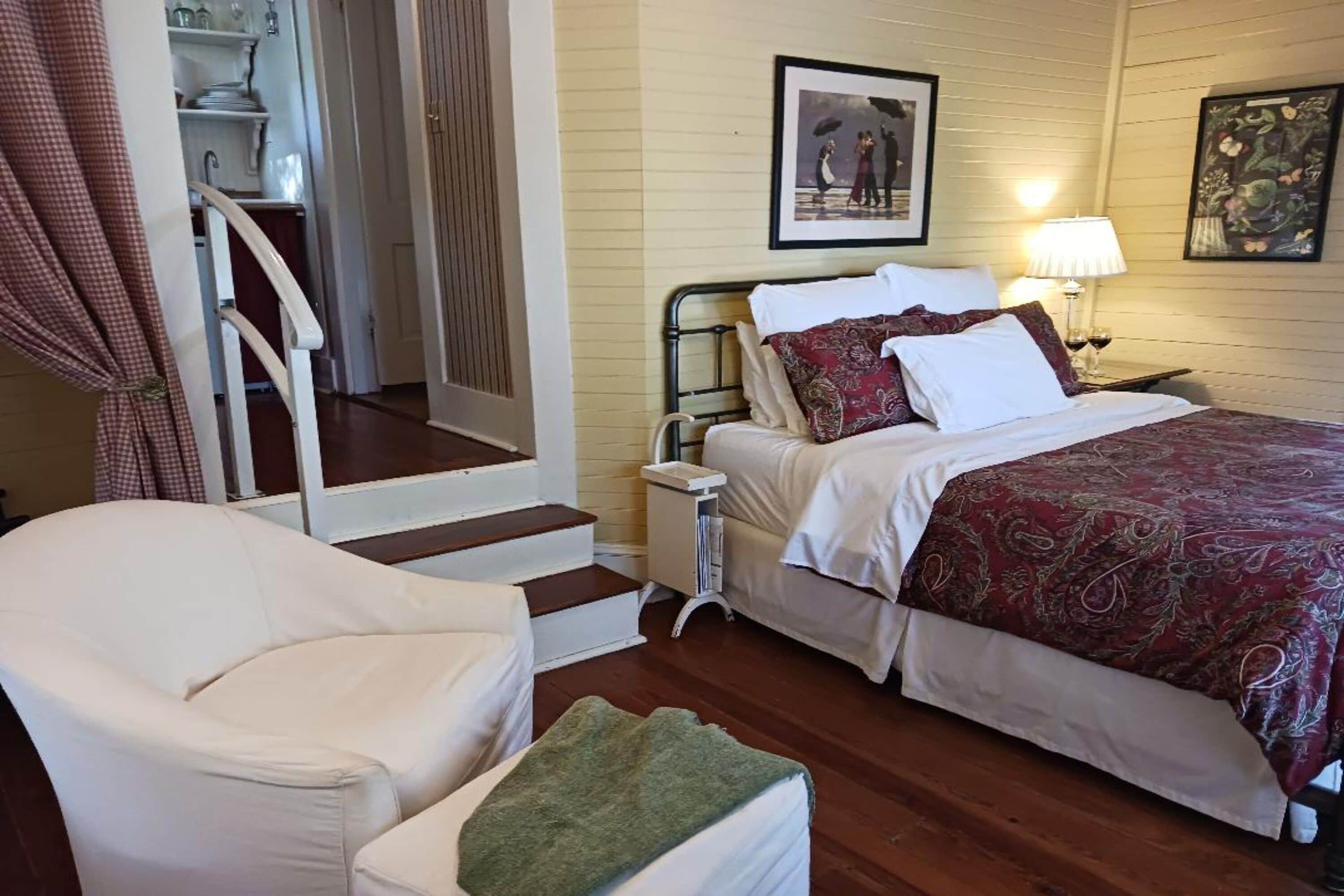 Un dormitorio con una cama, una silla, una mesita de noche y una escalera que lleva a una zona de cocina.