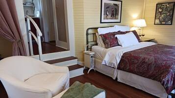 Un dormitorio con una cama, una silla, una mesita de noche y una escalera que lleva a una zona de cocina.