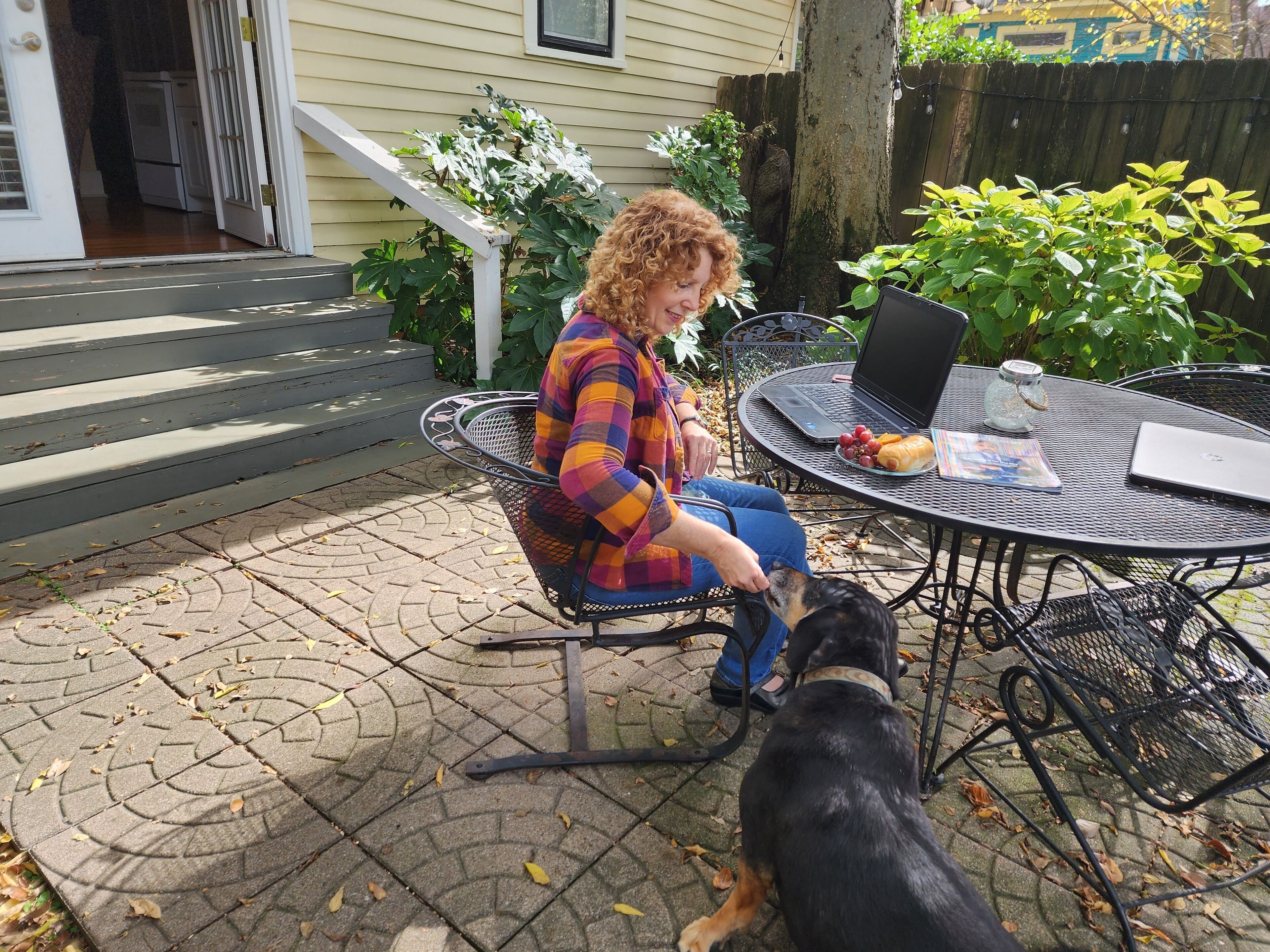 A person seated at a round metal table with a laptop, a glass jar, and a plate of grapes.