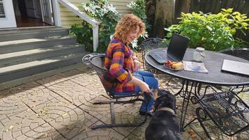 A person seated at a round metal table with a laptop, a glass jar, and a plate of grapes.