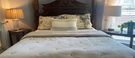 A neatly made bed with a wooden headboard, a bedside table with a lamp, and a window with blinds.
